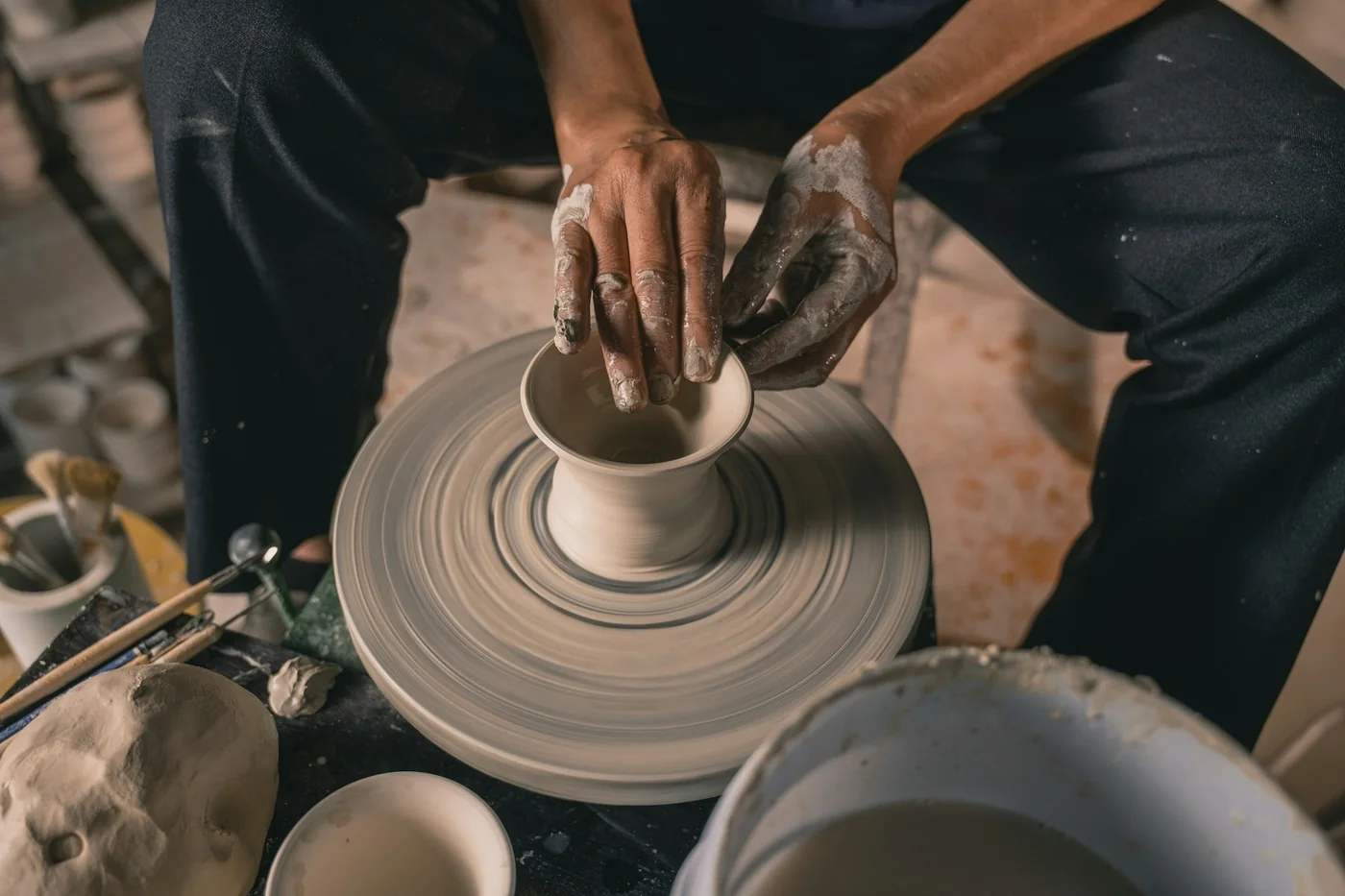 Hands shape a ceramic piece on a potter tower
